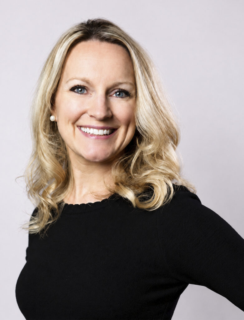 Smiling woman with blonde, curled hair wearing a black long sleeve shirt.